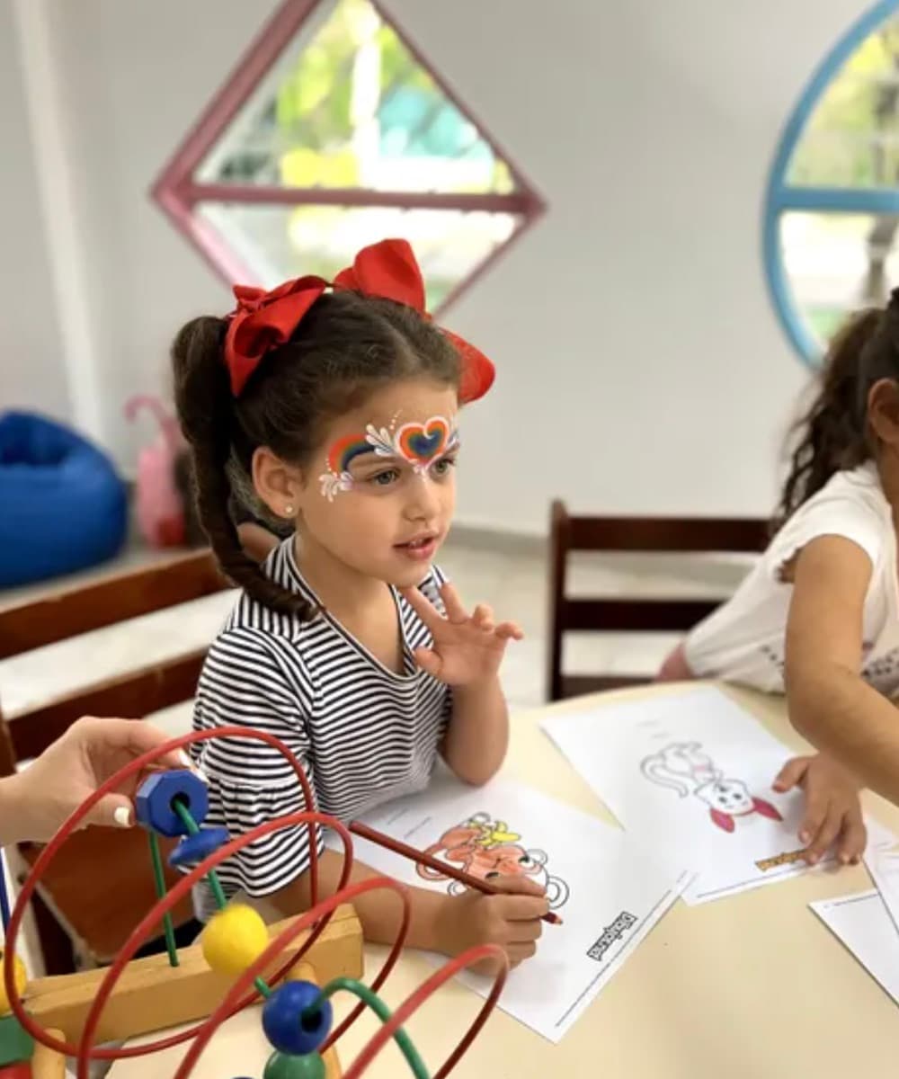 Niña con pintacaritas colorea durante la clase