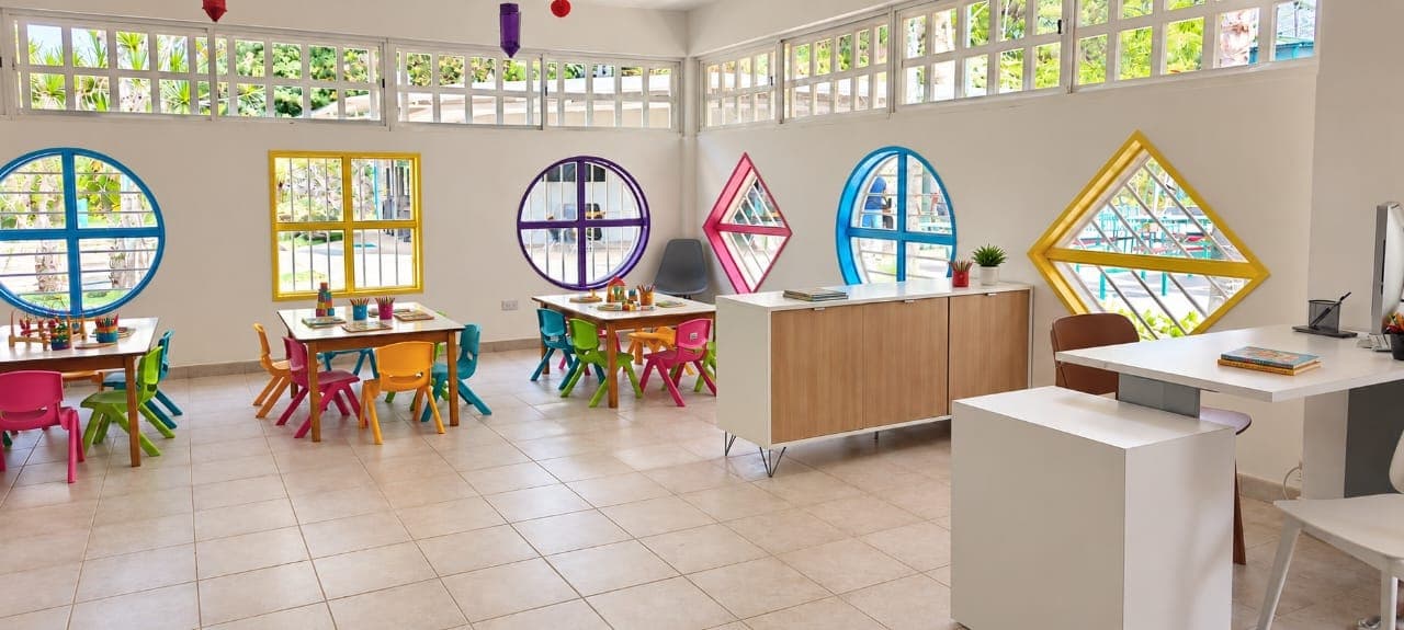 Aula luminosa de Italo Kids con ventanas en forma de círculo, cuadrado y rombo de colores, y mesas con sillas infantiles