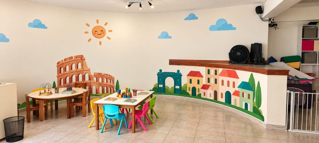 Mural pintado en la sede con el Coliseo, un arco y un pueblo italiano, junto a mesas de trabajo infantiles