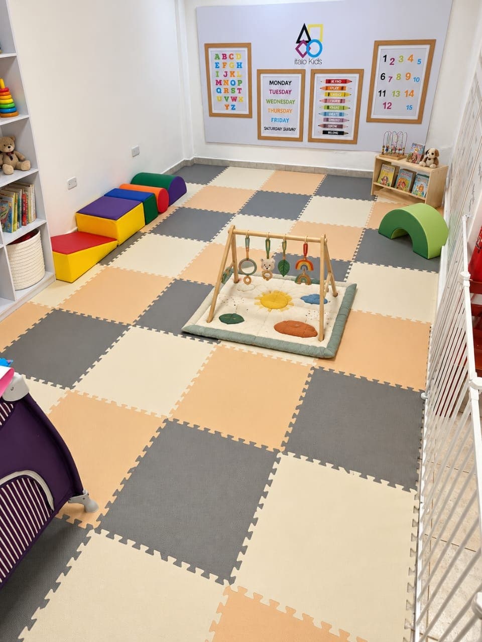 Sala de bebés con piso acolchado, gimnasio de madera, bloques de espuma y el logo de Italo Kids en la pared